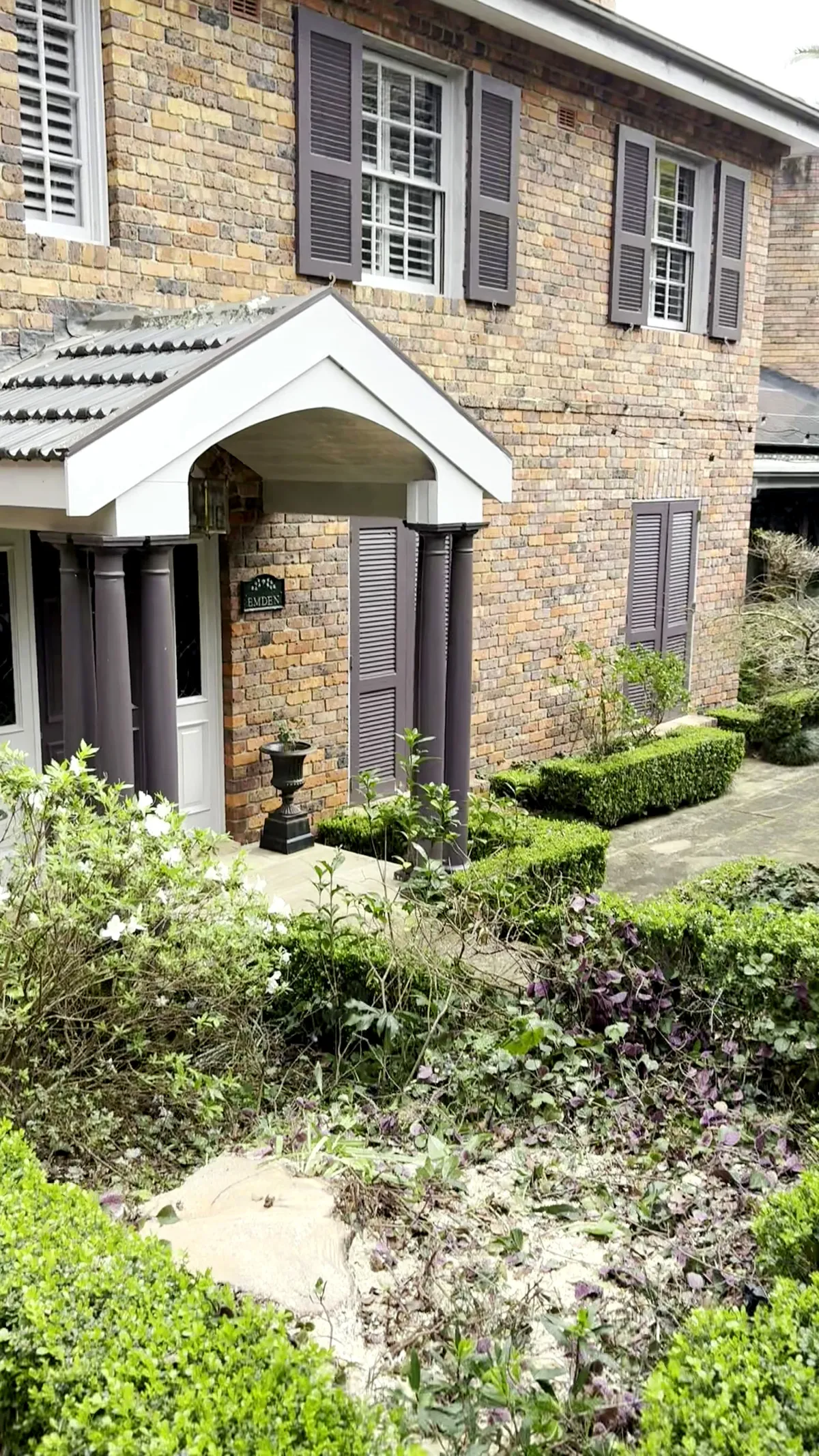The same brick house after, stump cut flush and the hedge and garden untouched